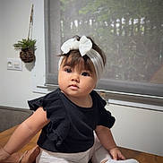 Louna participe au concours pour gagner de l'argent avec cette photo : baby, child, headband, bow, black_top, white_leggings, smiling_patch, white_shoes, table, indoor, window, plant, hand, cute, portrait, sitting, face, young_child, clothing, home