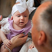 Ava is registered to the contest to win money with this photo: baby, child, infant, person, adult, headband, bow, lace, purple_clothing, hand, bracelet, indoor, family, affection, holding, portrait, closeup, soft_light, gentle, interaction