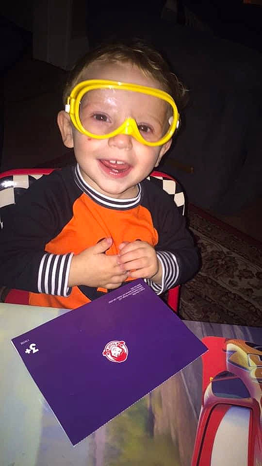 Jasper is registered to the contest to win money with this photo: baby, baby_toddler_clothing, carmine, child, costume, entertainment, event, eyewear, fun, goggles, happy, logo, orange, party, person, personal_protective_equipment, room, smile, t_shirt, toddler