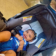 Khari is registered to the contest to win money with this photo: baby, child, infant, smiling, happy, portrait, car_seat, stroller, blue_outfit, hair_clips, curly_hair, sitting, indoors, travel, safety_harness, seat_belt, baby_gear, close_up, photography, family