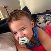 Ezra is registered to the contest to win money with this photo: toddler, child, pacifier, smiling, indoor, couch, pillow, blue_shirt, face, happy, relaxed, home, furniture, person, curly_hair, skin, portrait, young_child, casual, resting