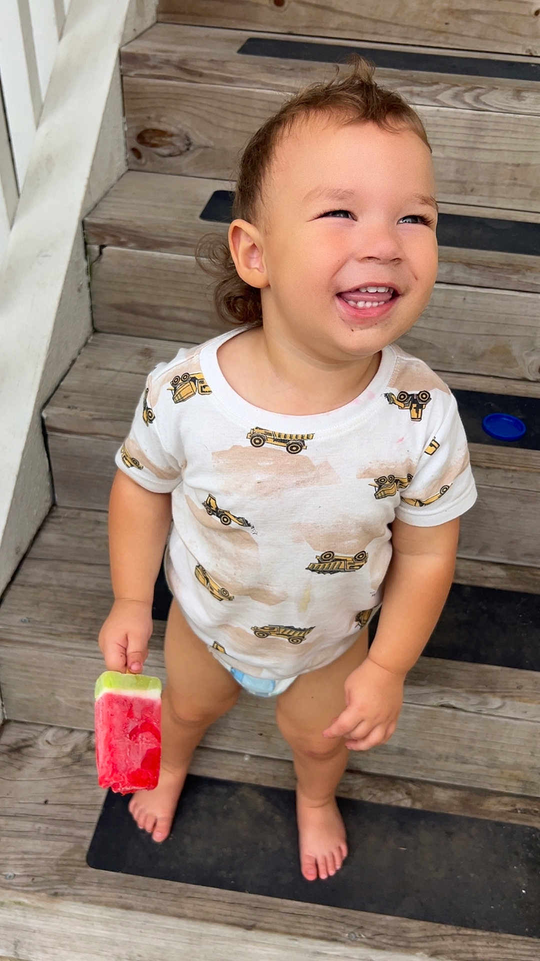 Ezra joined the competition — help win amazing prizes! toddler, child, smiling, popsicle, watermelon, barefoot, stairs, wooden_stairs, white_shirt, construction_vehicle_print, outdoor, happy, messy_shirt, summer, food, snack, cute, portrait, person, playful