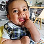 baby, child, smiling, face, hand, finger_in_mouth, plaid_clothing, button, short_sleeve, indoor, floor_tile, chair, table, lamp, toy, blanket, happy, cute, person, portrait