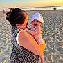 baby, beach, family, happy, hat, holding, nature, ocean, outdoor, person, sand, sky, smile, summer, sunlight, sunset, vacation, warm_light, water, woman