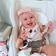 Malia participe au concours pour gagner de l'argent avec cette photo : baby, infant, high_chair, pink_headband, smiling, pacifier, toy, blanket, baby_clothes, indoor, cute, child, seat_belt, beads, soft_toy, happy, face, person, closeup, portrait
