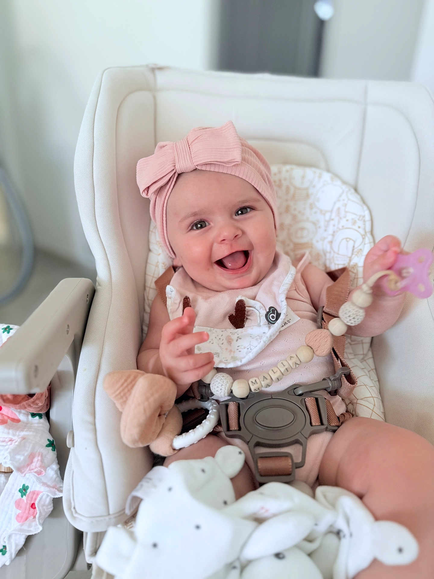 Malia participe au concours pour gagner de l'argent avec cette photo : baby, infant, high_chair, pink_headband, smiling, pacifier, toy, blanket, baby_clothes, indoor, cute, child, seat_belt, beads, soft_toy, happy, face, person, closeup, portrait