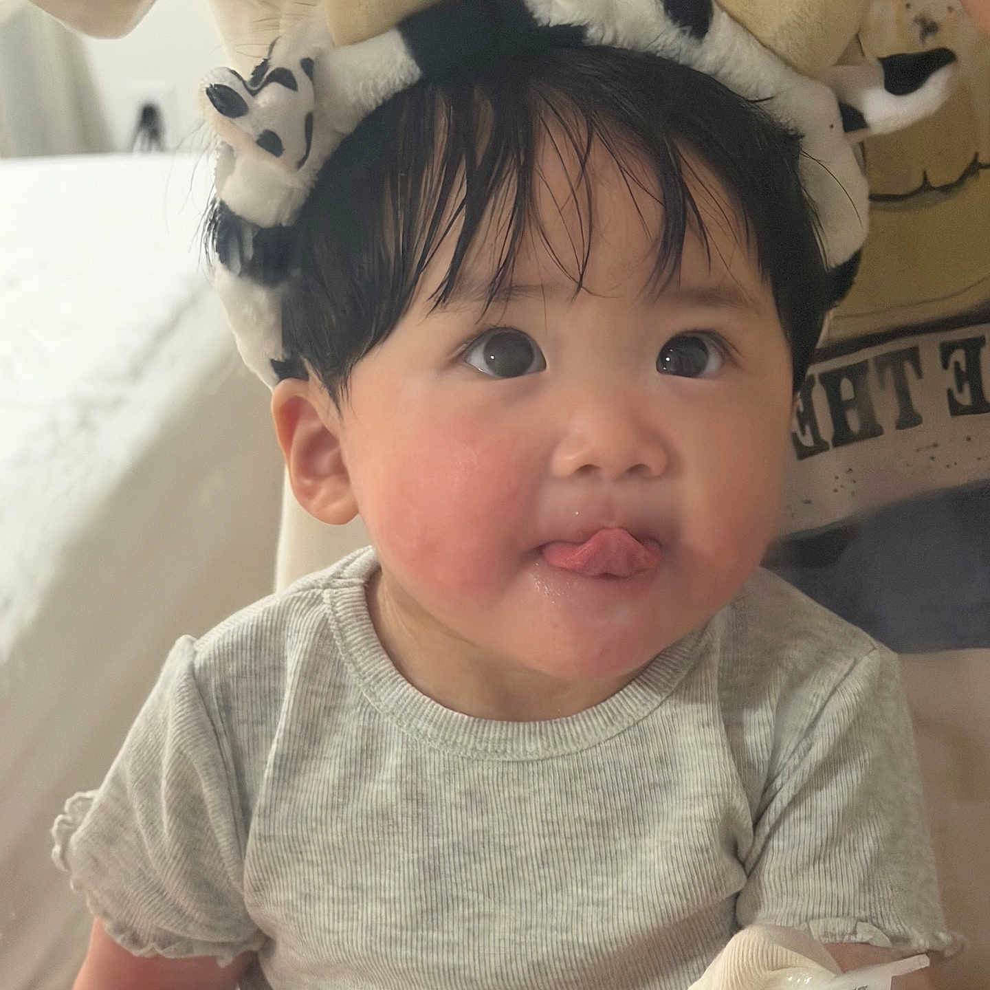 Kaylene is registered to the contest to win money with this photo: baby, child, tongue_out, headband, cow_pattern, horns, bandaged_hand, gray_shirt, indoor, cute, playful, face, person, young_child, portrait, sitting, soft_lighting, black_hair, skin, expression