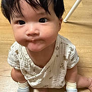 Kaylene is registered to the contest to win money with this photo: baby, child, infant, sitting, floor, wooden_floor, white_clothing, socks, cute, expression, indoor, person, young_child, looking_up, black_hair, small_hands, mischievous, patterned_clothing, closeup, portrait