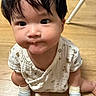 baby, child, infant, sitting, floor, wooden_floor, white_clothing, socks, cute, expression, indoor, person, young_child, looking_up, black_hair, small_hands, mischievous, patterned_clothing, closeup, portrait