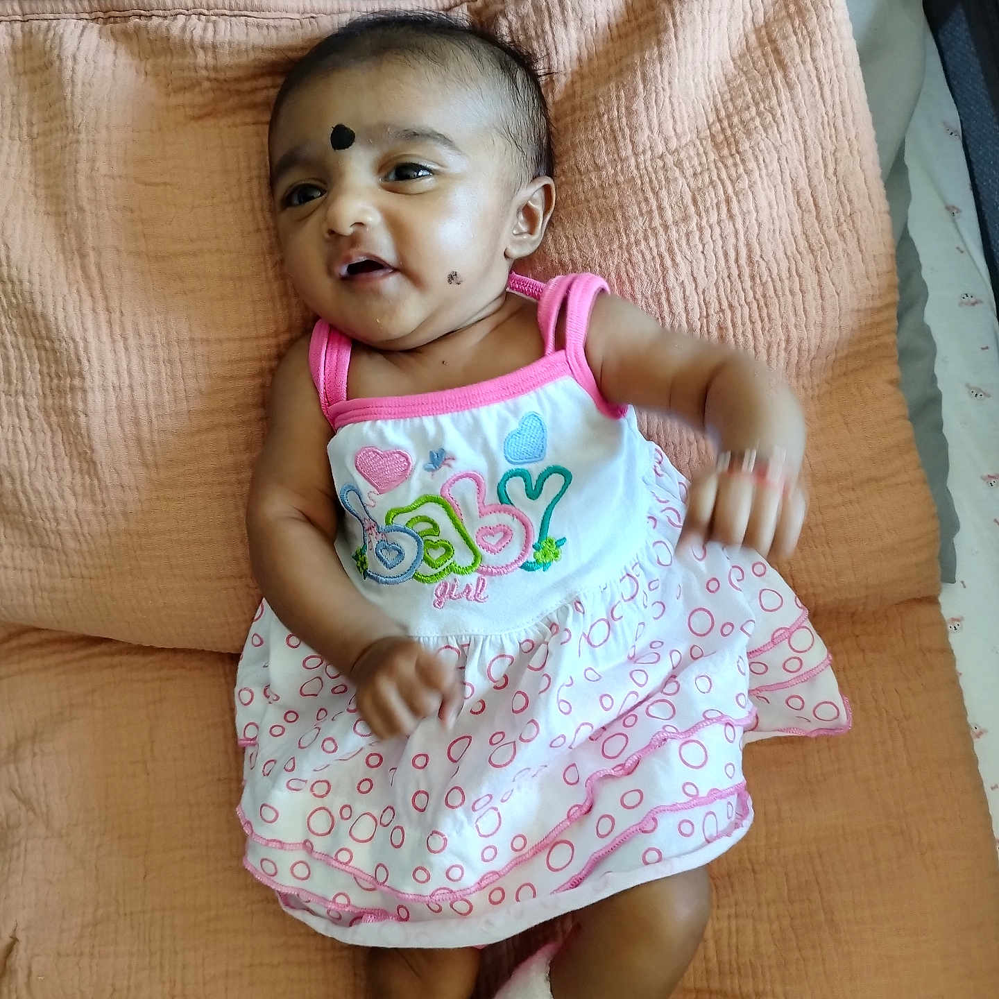 Athmika participe au concours pour gagner de l'argent avec cette photo : baby, bed, blanket, child, clothing, comfort, cute, dress, expression, face, indoors, infant, lying_down, person, pink, skin, sleepwear, sock, white, young