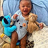 baby, smiling, blue_blanket, plush_toy, teddy_bear, blue_plush_dog, bottle, onesie, happy, infant, child, blanket, soft_toy, cute, lying_down, cheerful, indoors, face, person, cozy