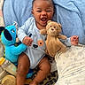 Thomas is registered to the contest to win money with this photo: baby, smiling, blue_onesie, stuffed_toy, teddy_bear, dinosaur_toy, blanket, baby_bottle, happy, infant, lying_down, cute, child, soft_toy, indoor, playful, cozy, face, hands, legs