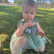 Louella joined the competition — help win amazing prizes! child, toddler, dress, green_dress, stick, grass, outdoor, nature, park, sunlight, blue_sky, fence, embroidery, barefoot, leaf, curious, sitting, person, young_child, summer