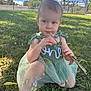 child, toddler, dress, green_dress, stick, grass, outdoor, nature, park, sunlight, blue_sky, fence, embroidery, barefoot, leaf, curious, sitting, person, young_child, summer