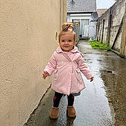 Alice a rejoint le concours — aidez-le/la à gagner de superbes lots ! toddler, child, pink_coat, standing, wet_ground, alleyway, puddle, outdoor, rainy, boots, topknot, smiling, concrete, building, wall, grass, satellite_dish, door, person, daylight