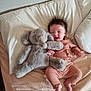 baby, infant, plush_toy, elephant_toy, bed, pillow, blanket, smiling, happy, child, soft_toys, cozy, cute, toddler, clothing, lying_down, indoors, person, sleepwear, furniture