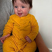 Edie joined the competition — help win amazing prizes! baby, infant, child, yellow_onesie, tongue_out, cute, playful, person, indoor, sitting, smiling, hair, blue_eyes, adult_arm, holding, clothing, face, skin, expression, happy
