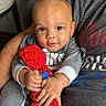 baby, child, plush_toy, spiderman, grey_clothing, person, arms, indoor, portrait, close_up, holding, cute, smiling, young_child, soft_toy, casual_wear, furniture, hand, face, comfort