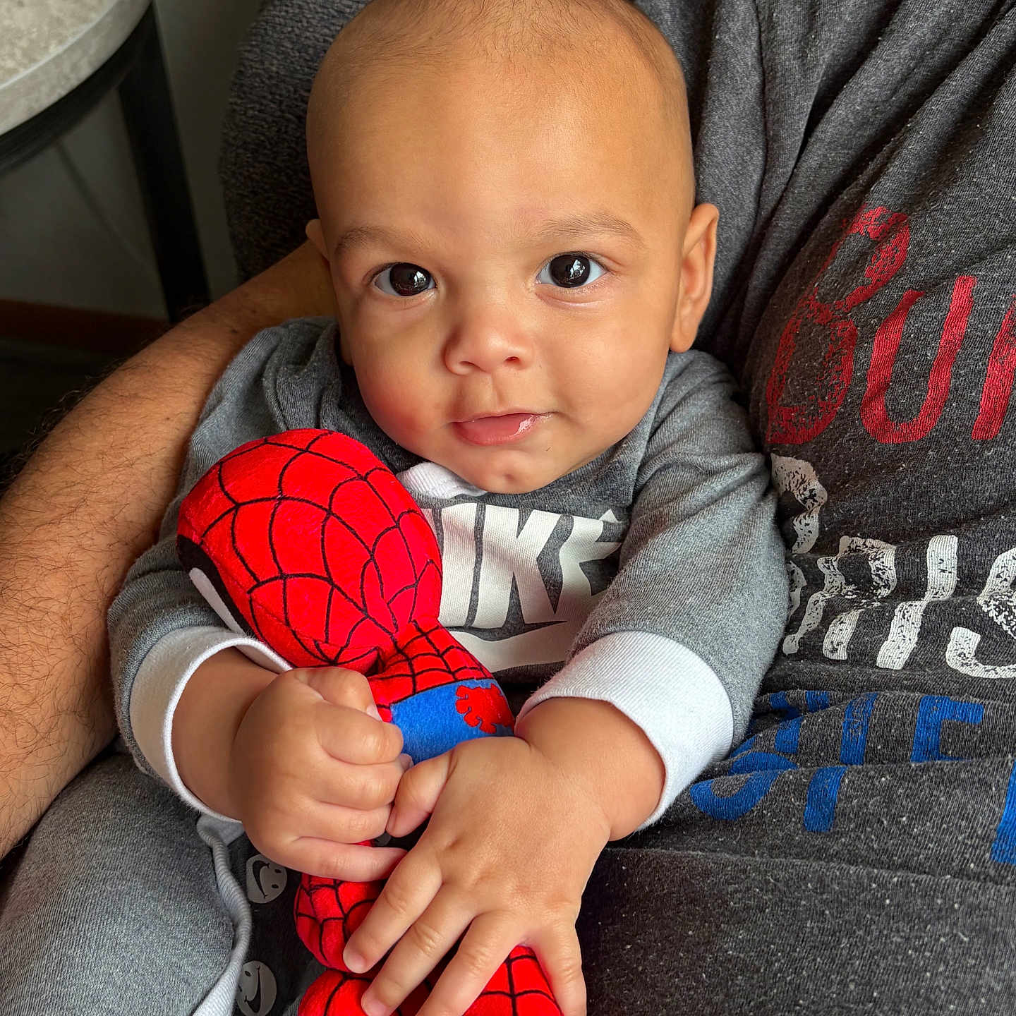 Apollo is registered to the contest to win money with this photo: baby, child, plush_toy, spiderman, grey_clothing, person, arms, indoor, portrait, close_up, holding, cute, smiling, young_child, soft_toy, casual_wear, furniture, hand, face, comfort