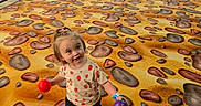 Paisleigh is registered to the contest to win money with this photo: balls, carpet, child, chocolate_chip_cookie_pattern, colorful, cute, fence, floor, happy, indoor, person, pink_socks, plants, play_area, playful, smiling, strawberry_shirt, toddler, windows, young_child