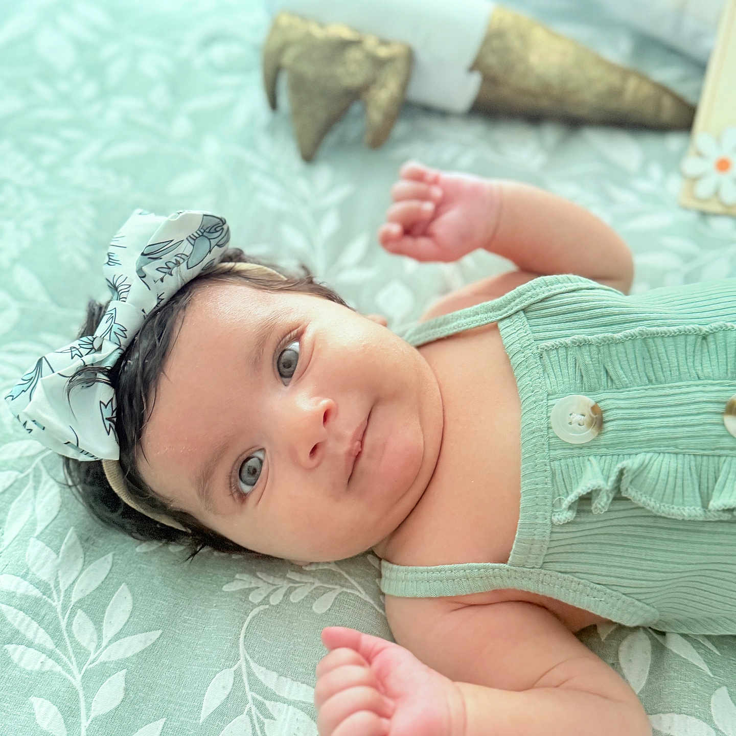 Kawsar joined the competition — help win amazing prizes! baby, background_blur, blanket, bow, buttons, child, cute, decor, eyes, face, fist, green_clothing, headband, indoor, infant, leaf_pattern, lying_down, pattern, skin, soft_light