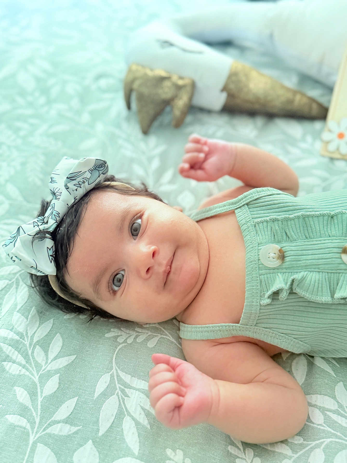 Kawsar joined the competition — help win amazing prizes! baby, infant, child, headband, bow, green_clothing, buttons, blanket, pattern, leaf_pattern, lying_down, fist, face, eyes, skin, cute, decor, background_blur, indoor, soft_light