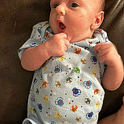 Cavan is registered to the contest to win money with this photo: baby, infant, onesie, clothing, cartoon, crab, blue, brown_leather, fist, curious, wide_eyes, skin, cute, laying_down, expression, young_child, person, indoors, child, newborn