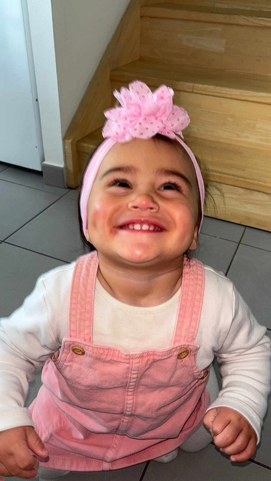 Harmonie a rejoint le concours — aidez-le/la à gagner de superbes lots ! toddler, child, smiling, pink_bow, headband, pink_overalls, white_shirt, dimples, teeth, happy, indoors, stairs, floor, tile, cute, baby, person, portrait, apparel, joyful