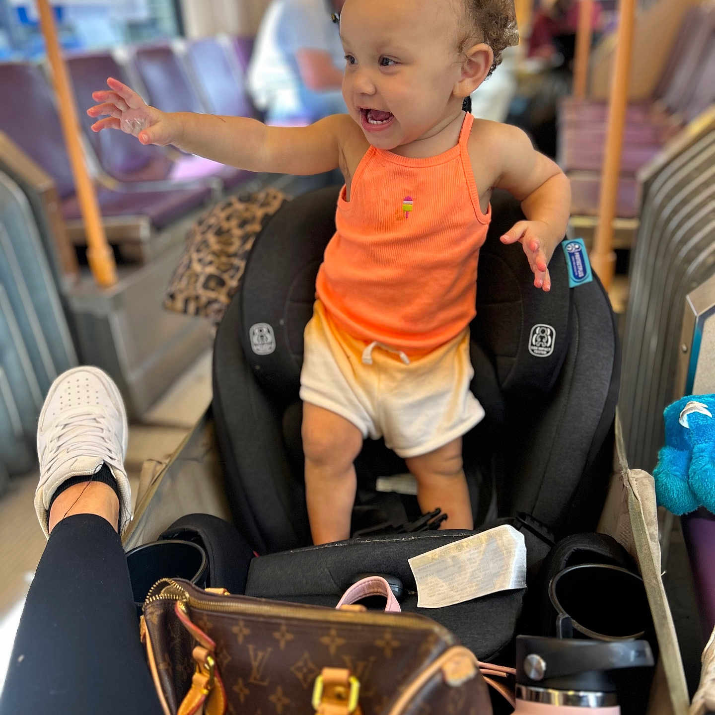 Ocianna joined the competition — help win amazing prizes! blurred_background, bus_interior, car_seat, child, clothing, curly_hair, handbag, happy, indoor, leg, orange_tank_top, person, public_transport, reaching, seat, sneaker, toddler, water_bottle, white_shorts, window
