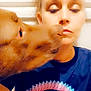 dog, person, dog_nose, kiss, t_shirt, logo, portrait, closeup, indoor, wall, hair, eyes_closed, snout, affectionate, blur, filter, human_face, pet, brown_dog, colorful_shirt