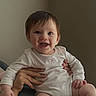 baby, child, infant, smiling, happy, portrait, face, person, indoor, home, seated, adult_hand, support, white_clothing, long_sleeves, brown_hair, eyes, chair, close_up, photography