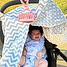 Alanna joined the competition — help win amazing prizes! baby, infant, child, stroller, smiling, outdoor, park, blanket, pink_toy, canopy, grass, sunlight, portrait, face, clothing, dress, seated, happy, chevron_pattern, polka_dot