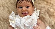 Alanna is registered to the contest to win money with this photo: baby, child, infant, smiling, portrait, headband, bow, white_dress, eyelet_fabric, sitting, blanket, woven_texture, indoors, close_up, face, hands, brown_hair, happy, baby_fashion, cozy