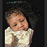 baby, infant, child, portrait, face, eyes, curly_hair, dark_hair, sleepy, calm, looking_at_camera, close_up, swaddled, blanket, patterned_clothing, indoors, dark_background, photography, head, newborn