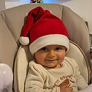 Matteo participe au concours pour gagner de l'argent avec cette photo : baby, child, santa_hat, high_chair, smile, indoor, christmas_tree, holiday, festive, television, blurred_background, cozy, clothing, seat, infant, cute, face, portrait, holiday_season, celebration