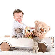 Joachim participe au concours pour gagner de l'argent avec cette photo : child, baby, toddler, smiling, wooden_car, toy_car, teddy_bear, stuffed_toy, plush_toy, knitted_bunny, flower, white_background, studio, portrait, sitting, happy, cozy, fur_rug, decorative, cute