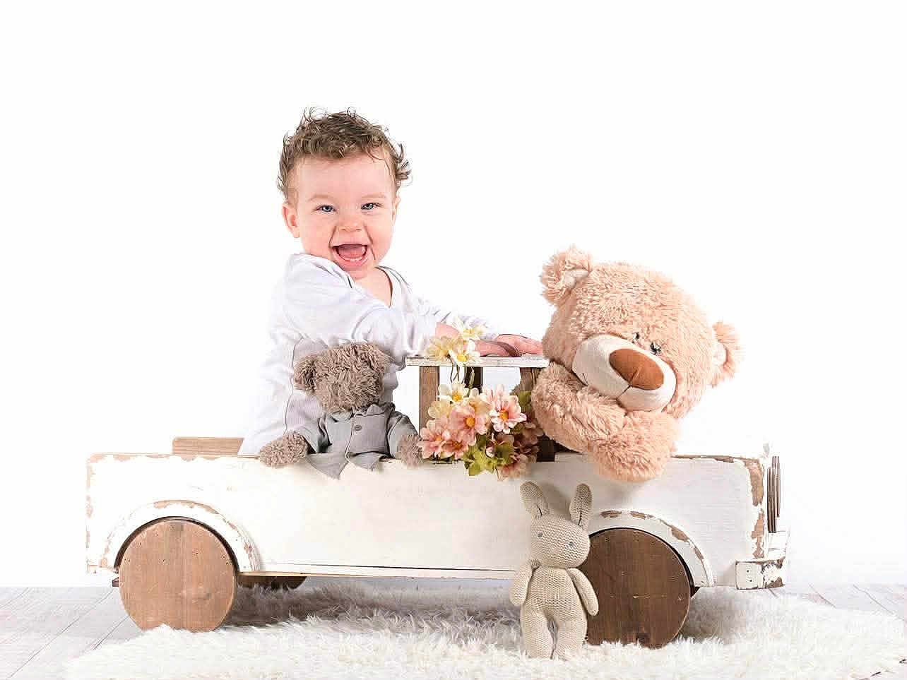 Joachim participe au concours pour gagner de l'argent avec cette photo : child, baby, toddler, smiling, wooden_car, toy_car, teddy_bear, stuffed_toy, plush_toy, knitted_bunny, flower, white_background, studio, portrait, sitting, happy, cozy, fur_rug, decorative, cute
