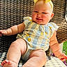 baby, child, smiling, yellow_bow, romper, striped_clothing, lemon_print, wicker_chair, checkered_cushion, outdoor, greenery, sunlight, cute, happy, infant, seated, plump_legs, headband, portrait, summer