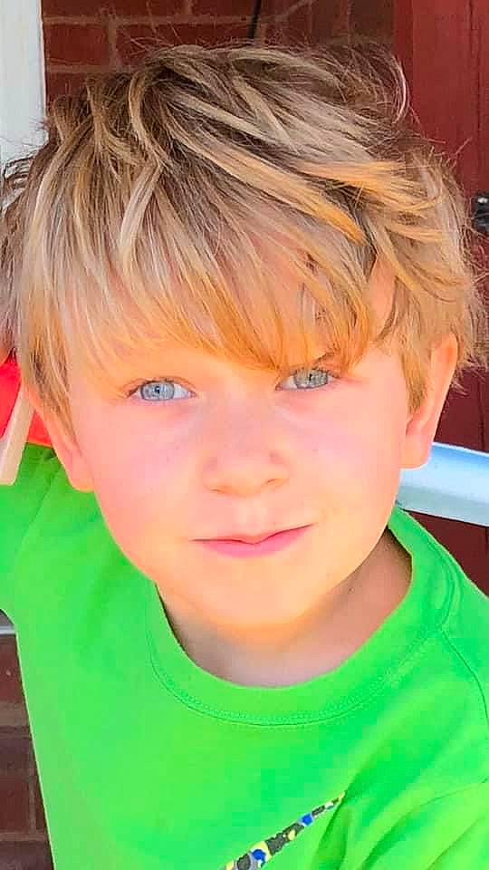 Merrick is registered to the contest to win money with this photo: bangs, blond, cheek, chin, eyebrow, eyelash, face, forehead, happy, iris, jaw, mouth, neck, nose, person, sleeve, smile, surfer_hair, t_shirt, toddler
