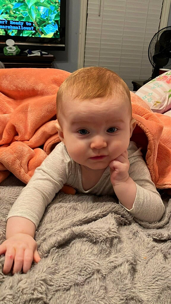 Caroline is registered to the contest to win money with this photo: baby, baby_toddler_clothing, cable_television, cheek, chin, comfort, couch, finger, floor, flooring, iris, mammal, nose, person, skin, sleeve, smile, television, toddler, vertebrate