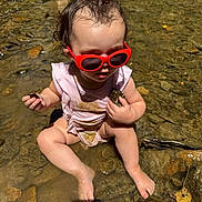 Brynleigh is registered to the contest to win money with this photo: toddler, child, red_sunglasses, water, rocks, stream, muddy_clothes, wet_hair, sitting, barefoot, outdoor, nature, summer, curly_hair, person, exploring, play, sunlight, shallow_water, legs