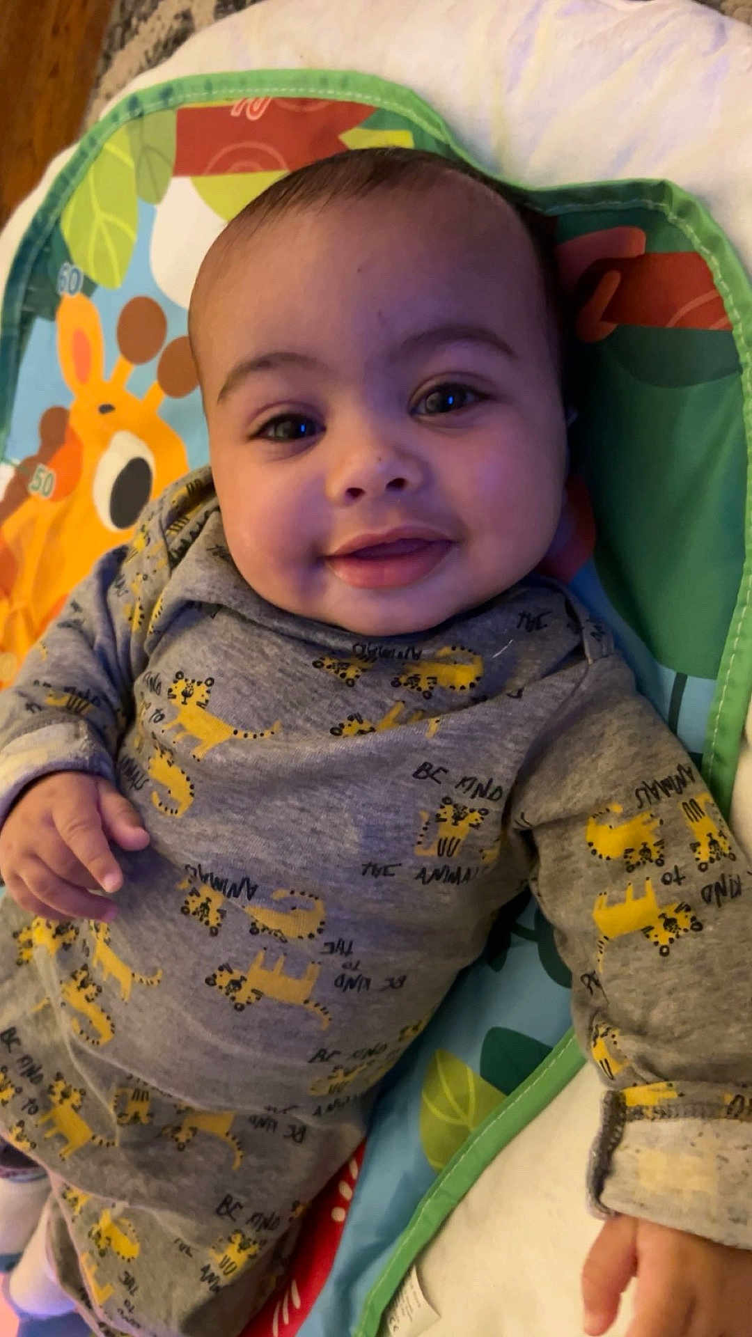Zylo joined the competition — help win amazing prizes! baby, smiling, infant, face, clothing, grey_outfit, yellow_cheetah_prints, hand, play_mat, giraffe, colorful, lying_down, cute, child, indoors, portrait, young, happy, person, soft_lighting