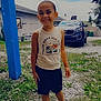 child, smiling, outdoor, grass, gravel, car, blue_post, shorts, sleeveless_shirt, sandals, happy, person, nature, daytime, cloudy_sky, house, tree, portrait, casual_clothing, young