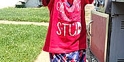 Daelyne is registered to the contest to win money with this photo: child, smiling, outdoor, grass, sidewalk, red_shirt, colorful_shorts, happy, person, grill, house, stairs, sunny, daylight, footwear, sock, patterned_clothing, reaching, playful, portrait