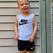 Jace joined the competition — help win amazing prizes! child, boy, smiling, tank_top, shorts, nike, outdoor, wall, wooden_wall, standing, happy, casual_clothing, young, person, summer, daylight, barefoot, portrait, cute, fashion