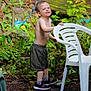 Jace is registered to the contest to win money with this photo: child, boy, outdoor, garden, plants, greenery, plastic_chair, sneakers, shorts, shirtless, smile, wet, dirt, tree, wagon_wheel, playful, nature, young, happy, person