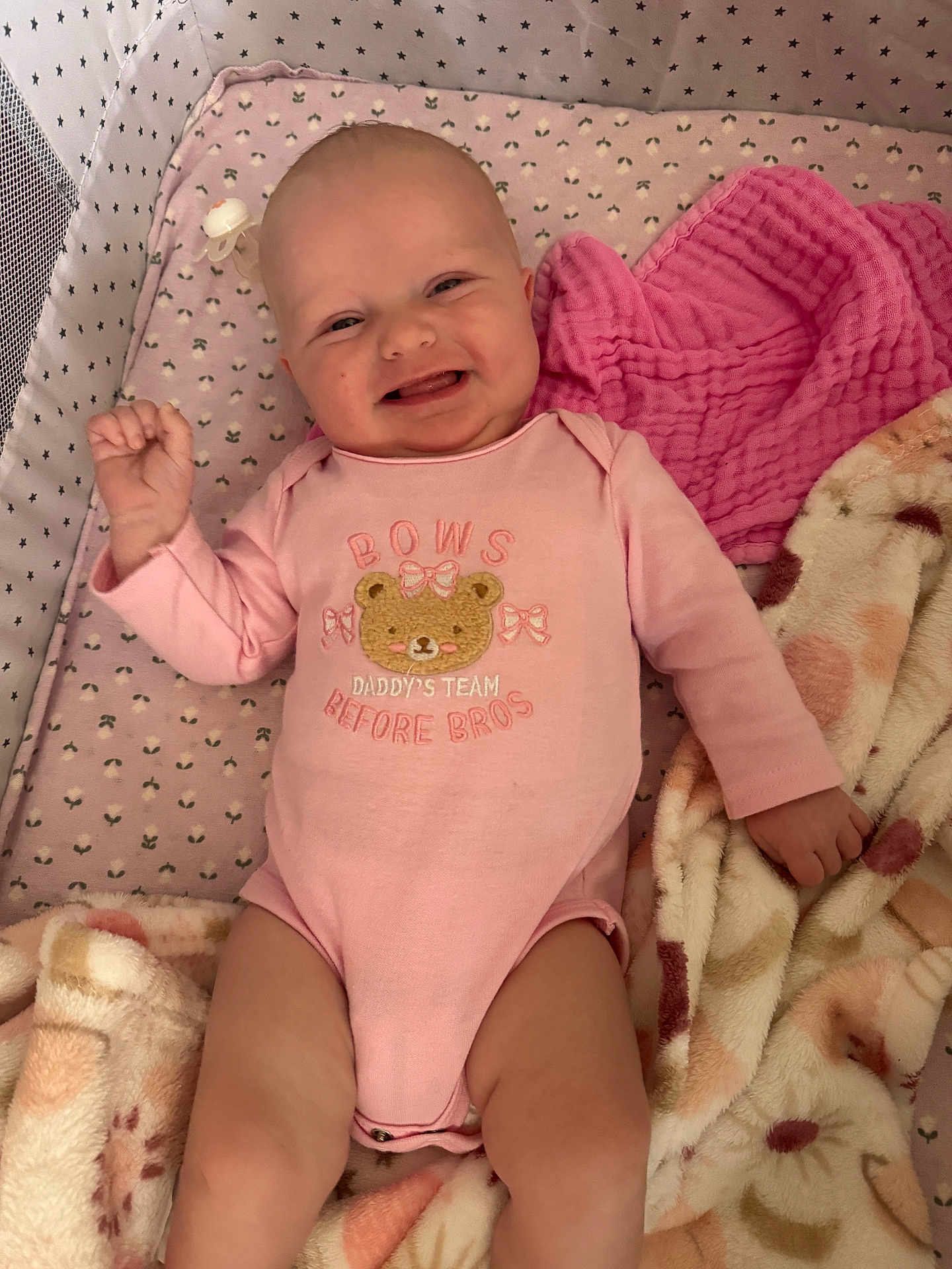 Scarlette is registered to the contest to win money with this photo: baby, infant, smiling, onesie, pink_clothing, crib, blanket, pacifier, face, skin, child, cute, happy, lying_down, soft_texture, patterned_blanket, sleeping_area, baby_girl, indoors, cozy