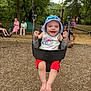 Knox is registered to the contest to win money with this photo: baby, child, swing, playground, hat, smile, happy, outdoor, trees, bench, people, park, grass, woodchips, summer, clothing, feet, chain, fun, daylight
