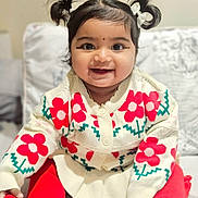 Iza is registered to the contest to win money with this photo: baby, child, smiling, pigtails, sweater, red_flowers, red_tights, sitting, indoors, couch, cozy, cute, portrait, happy, face, person, young_child, warm_clothing, home, infant