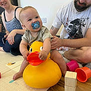 Ryder is registered to the contest to win money with this photo: baby, pacifier, rubber_duck, toy, wooden_blocks, colorful_cups, floor_mat, adult, man, woman, smile, indoor, child, playtime, family, happy, sitting, clothing, beard, tattoo